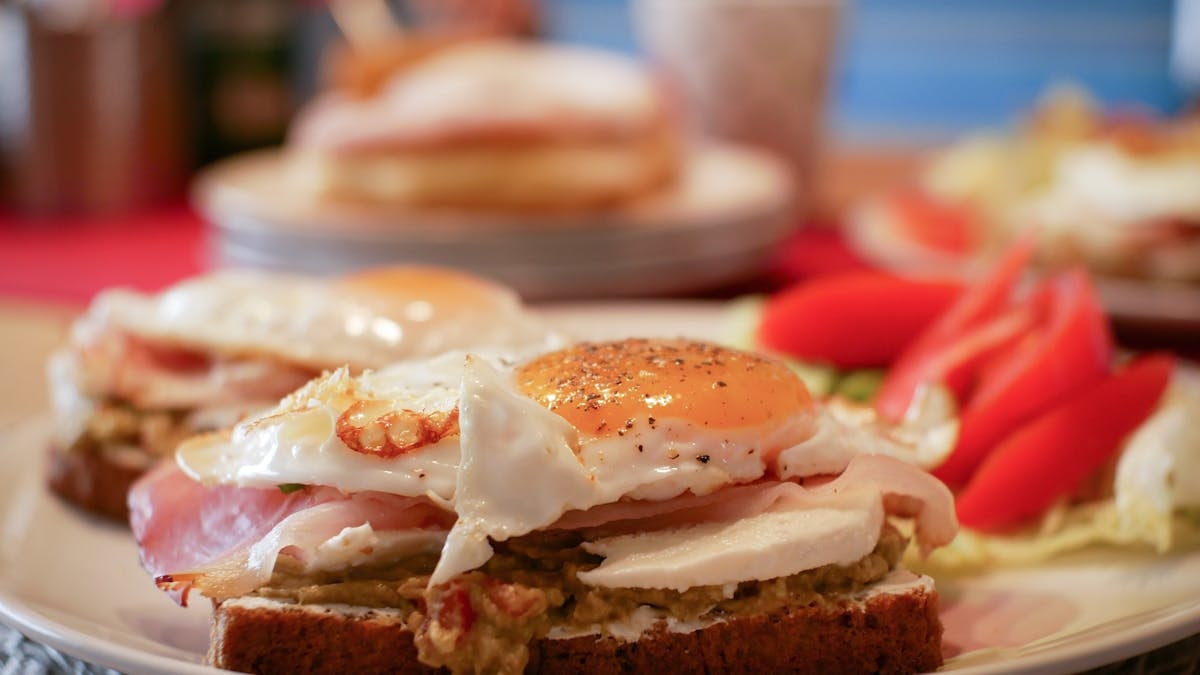 Close-up of a savory breakfast with fried eggs, avocado, and ham on toast.